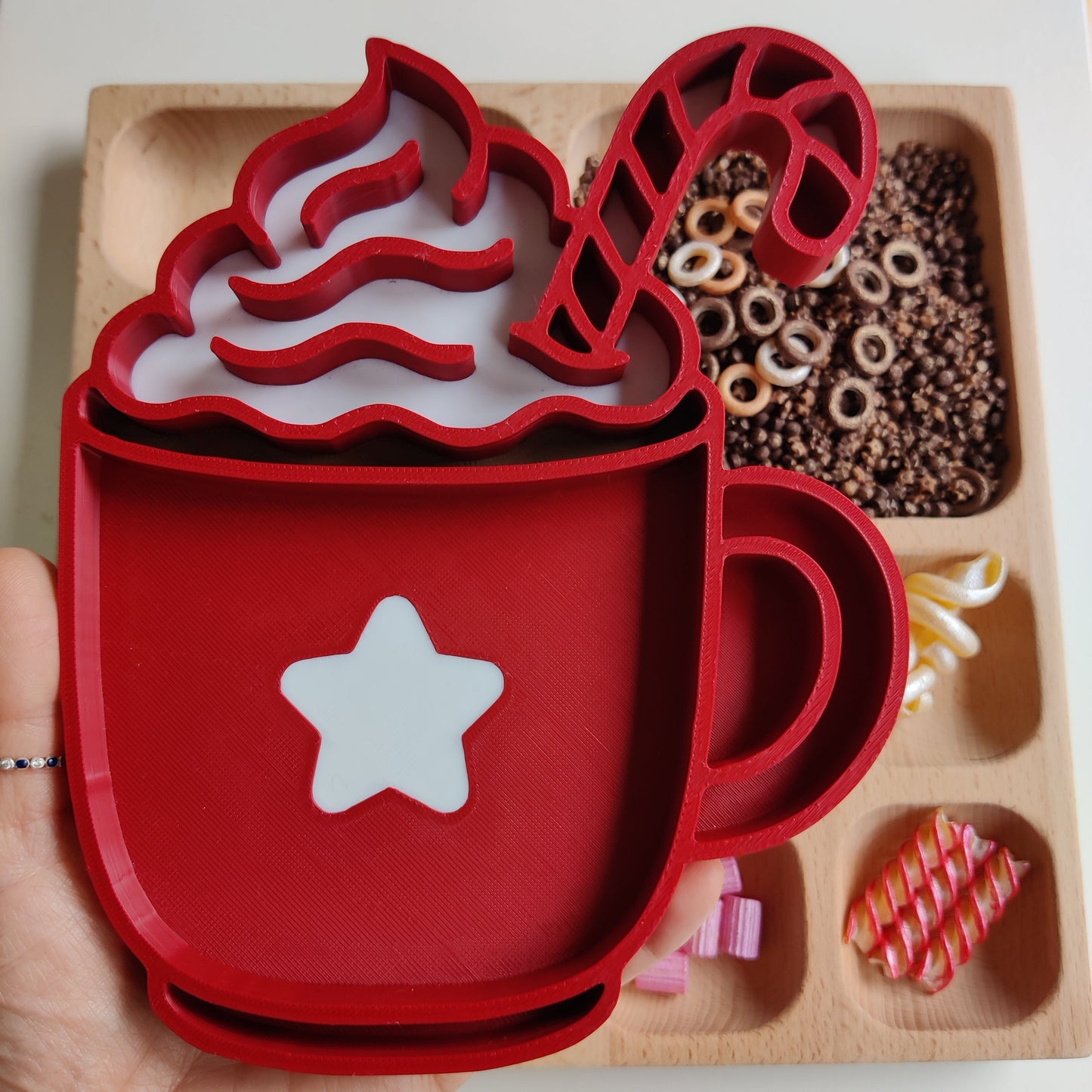 Red hot chocolate-themed cookie cutter set on a wooden tray with candy pieces.