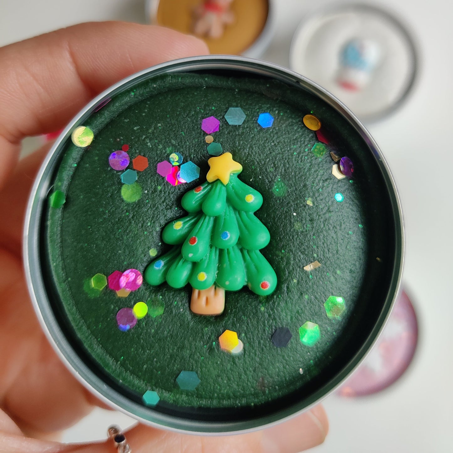 xmas themed Sensory Play doughs Hand holding a small green Christmas tree decoration on a dark surface with colorful confetti.