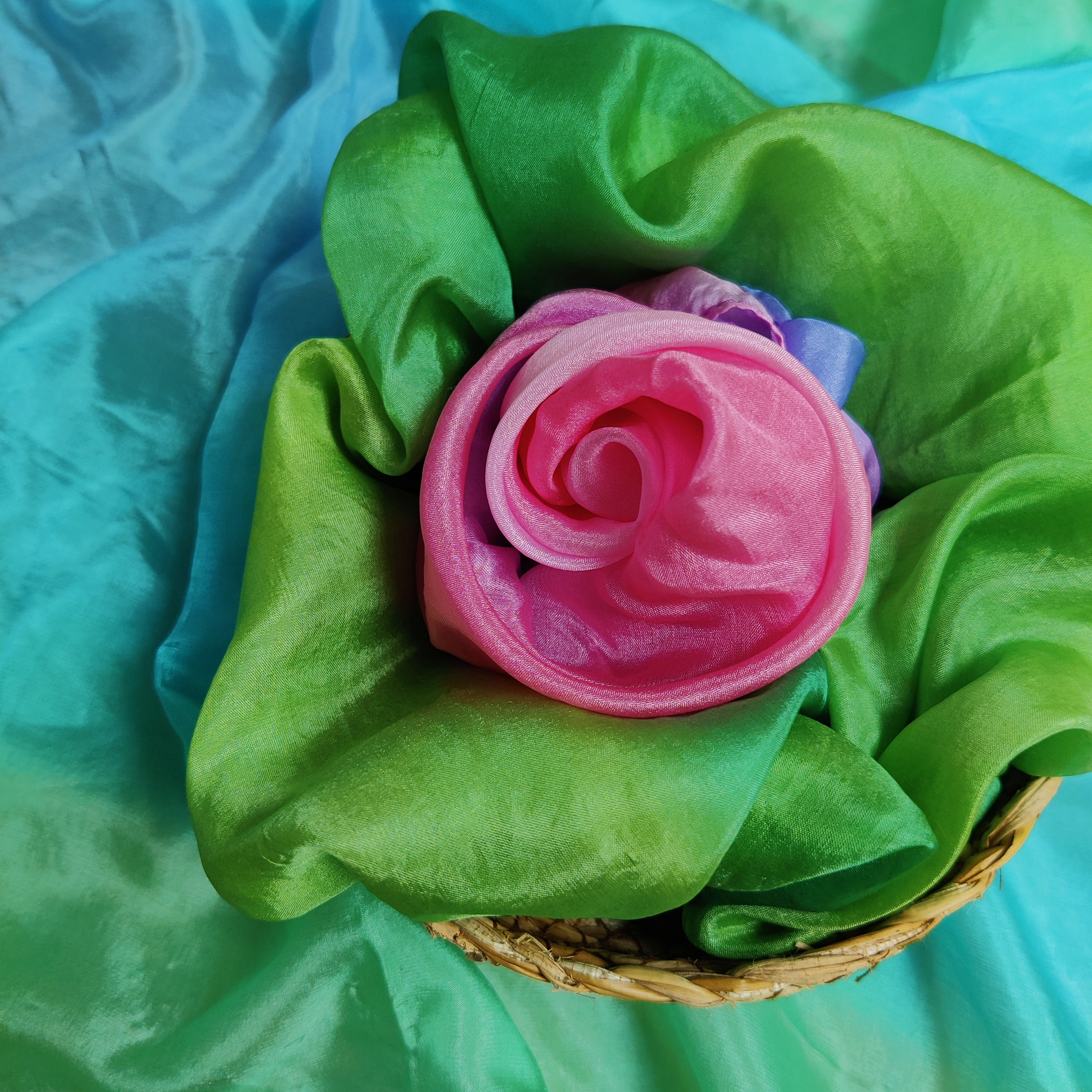 Pink flower-shaped play silk on green fabric with a blue background
